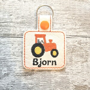 May include: A white leather keychain with an orange tractor design and the name "Bjorn" embroidered in black thread.
