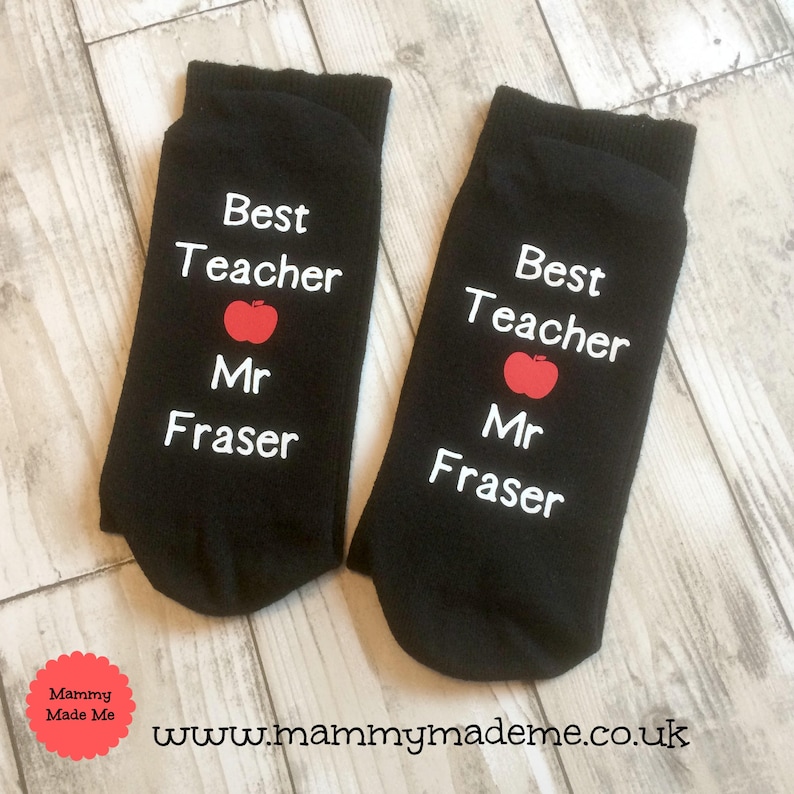 May include: Pair of black socks with white text that reads "Best Teacher Mr. Fraser" and a red apple graphic.