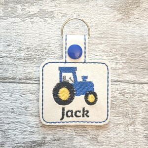 May include: A white leather keychain with a blue tractor design and the name "Jack" embroidered on it.