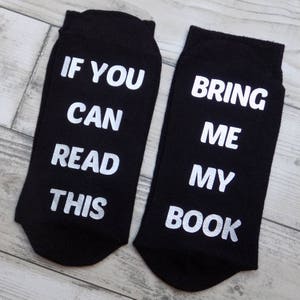 Op de afbeelding: Een paar zwarte sokken met witte tekst. E&eacute;n sok zegt "Als je dit kunt lezen" en de andere sok zegt "Breng me mijn boek".