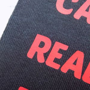 Op de afbeelding: Close-up van een zwarte stof met het woord "REAL" in rood gedrukt.