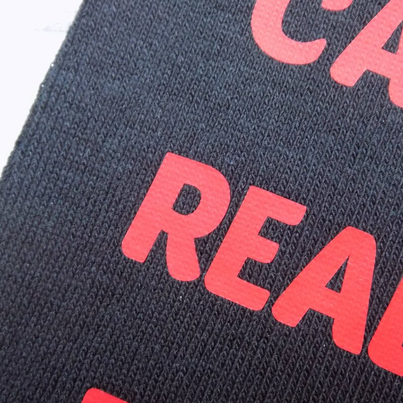 Op de afbeelding: Close-up van een zwarte stof met het woord "REAL" in rood gedrukt.