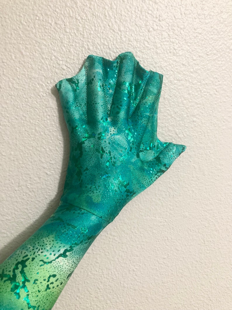 May include: A green and blue mermaid fin glove with a sparkly finish. The glove has a scalloped edge and is made of a stretchy fabric.