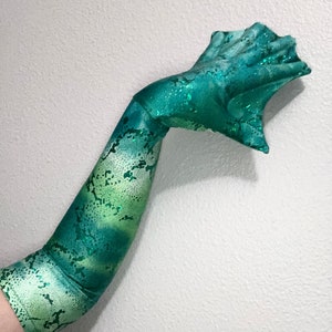 May include: A long, green and white arm sleeve with a glittery finish. The sleeve has a snake skin pattern and is made of a stretchy fabric.