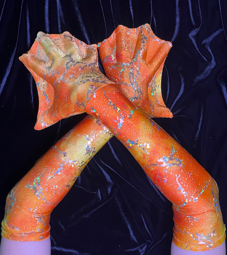 May include: A pair of orange and gold glittery fingerless gloves with a mermaid tail design at the wrist.