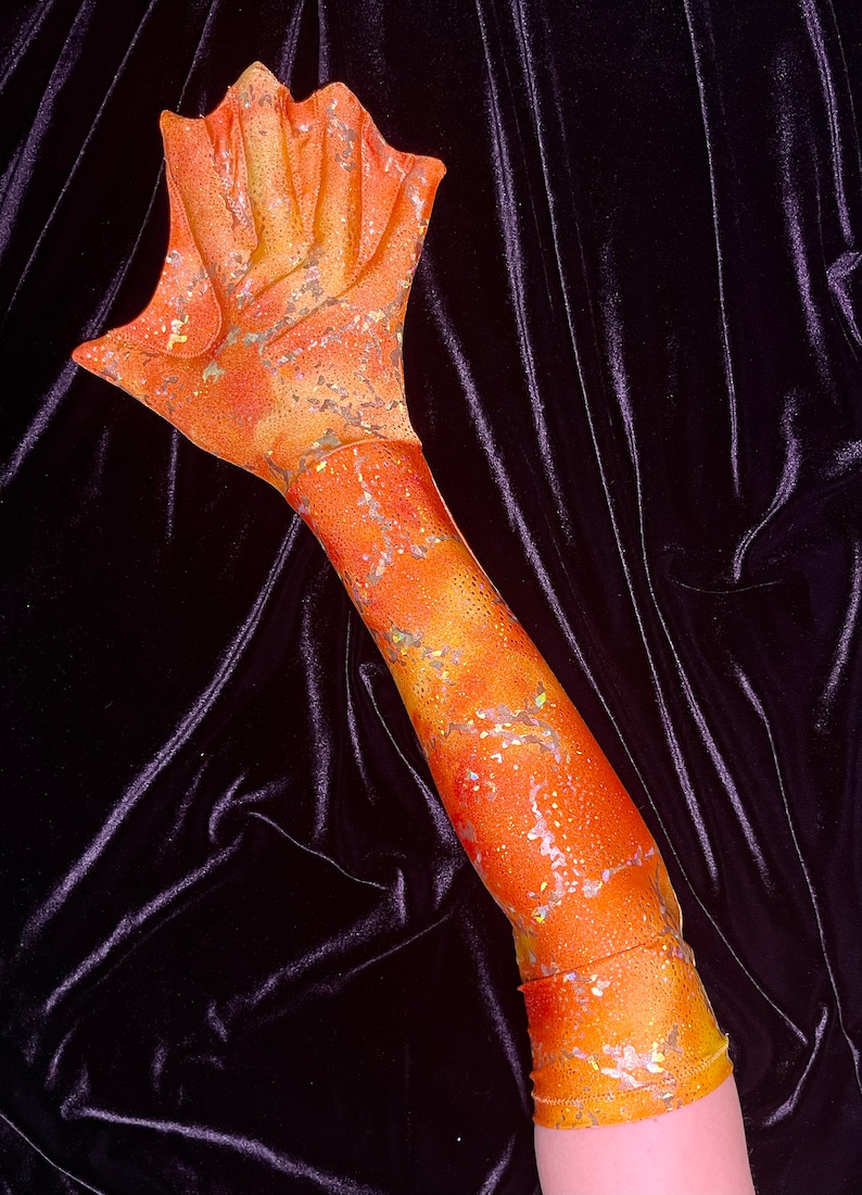 May include: A long orange and gold arm sleeve with a glittery finish. The sleeve has a textured pattern and is made of a stretchy fabric.