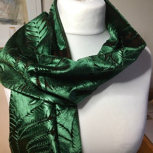May include: A green velvet scarf with an embossed leaf pattern. The scarf is folded and draped over a white mannequin.