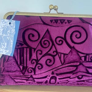 Peut inclure: Une pochette en velours violet foncé avec un fermoir en laiton. La pochette présente un motif abstrait noir en relief. Une étiquette bleu clair est attachée avec le texte "Kim M. McCormack Textiles & Scottish Highlands."