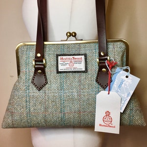 Bolso de mano escocés Harris Tweed con cierre de boquilla en un estampado de espiga en verde azulado claro con asas de cuero.