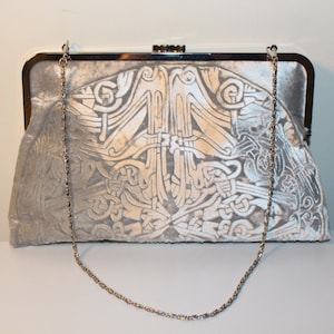 A silver kisslock clutch bag in an embossed iridescent velvet celtic design