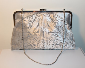 A silver kisslock clutch bag in an embossed iridescent velvet celtic design