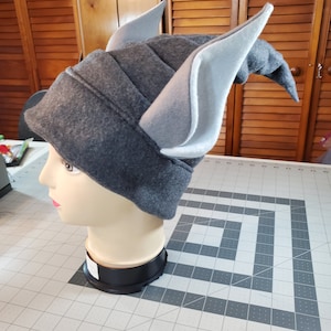 May include: Gray fleece hat with large, pointed, gray and white ears. The hat is on a mannequin head.