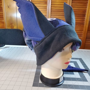 May include: A black and blue fleece hat with large, pointed ears. The hat is on a mannequin head.