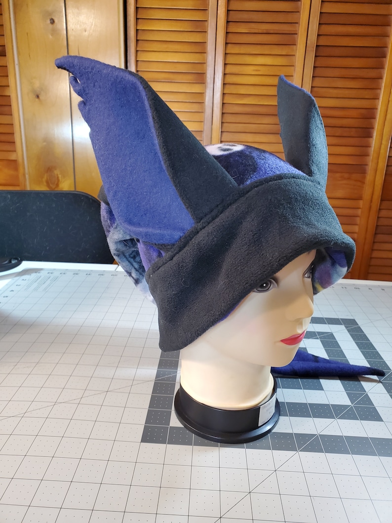 May include: A black and blue fleece hat with large, pointed ears. The hat is on a mannequin head.