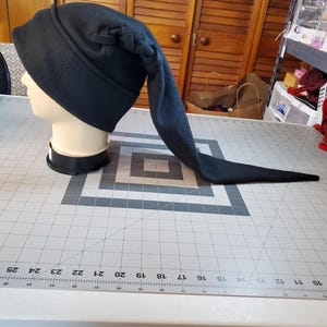 Puede incluir: Un gorro de lana negro con una cola larga. El gorro tiene un detalle trenzado en la parte superior.