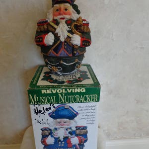 May include: A hand-painted poly-stone musical nutcracker figurine in a blue and red uniform with gold trim. The nutcracker is in a box that says "Revolving Musical Nutcracker" and "Holiday Traditions Collectible".