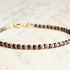 May include: A delicate bracelet made with small brown and gold beads. The bracelet has a simple clasp closure.
