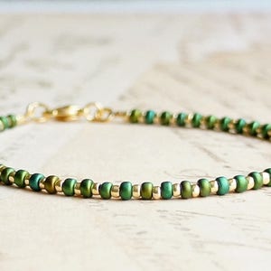 May include: A delicate green and gold beaded bracelet with a clasp fastening.
