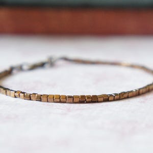May include: A simple bracelet made of small, square, copper-colored beads.