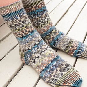 Puede incluir: Un par de calcetines con estampado colorido con un diseño geométrico en tonos azules, grises, verdes y naranjas. Los calcetines están hechos de un tejido suave de punto.