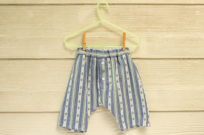May include: Blue and white striped pants with a green pattern hanging on a light green hanger. The pants have a button closure and a drawstring waist.