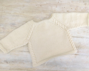 May include: A cream-colored knitted sweater with a cable knit design on the sleeves and neckline.