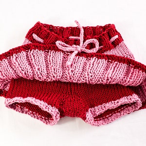 May include: A red and pink knitted skirt with a ruffled hem and a tied bow at the waist.