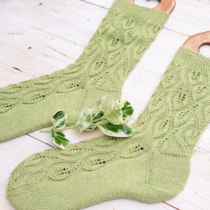 Può includere: Un paio di calze di lana verde con un motivo a pizzo. Le calze sono esposte su blocchi di calze in legno.