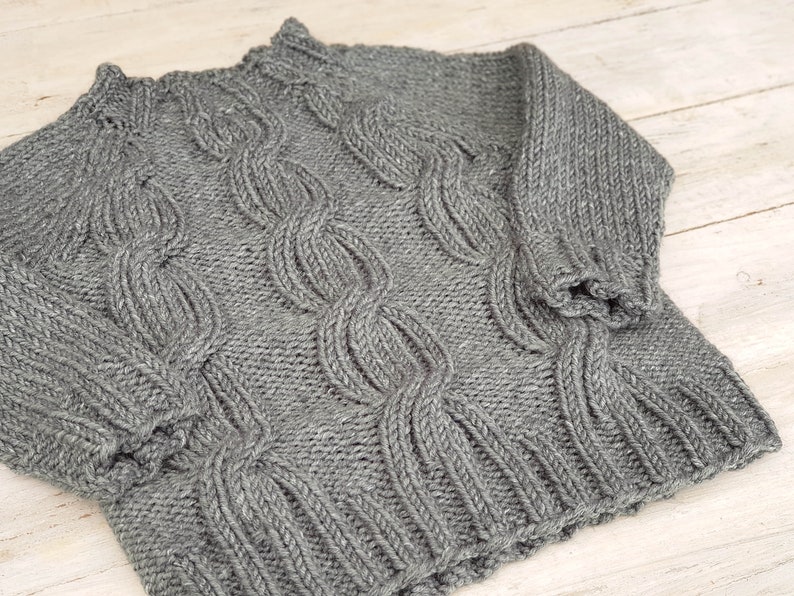 May include: A gray knitted sweater with a cable knit pattern.