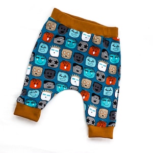 May include: Blue and orange baby pants with a pattern of colorful faces. The pants have a brown elastic waistband.