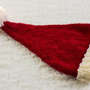 Può includere: Un cappello di Babbo Natale rosso lavorato a maglia con un pon pon bianco e un bordo bianco.