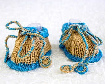 May include: A pair of knitted baby booties with a brown and blue color scheme. The booties have a tie at the top and a small button on the side.