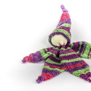 May include: A handmade knitted doll with a purple, green, and pink striped outfit and a pointed hat. The doll has a white fabric face.