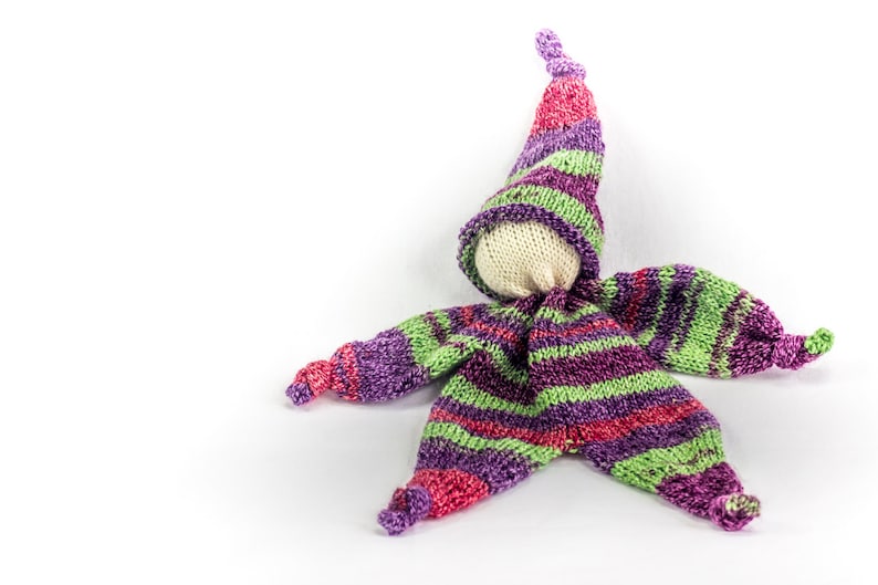 May include: A handmade knitted doll with a purple, green, and pink striped outfit and a pointed hat. The doll has a white fabric face.