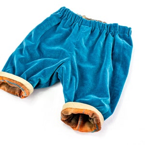 Op de afbeelding: Blauwe fluwelen shorts met een contrasterende oranje en bruine geruite bies rond de tailleband en de pijpen.