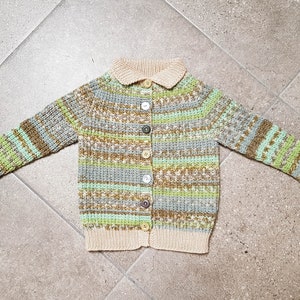 May include: A knitted cardigan with a striped pattern in shades of green, brown, and beige. The cardigan has a button-up front and a collar.