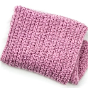 Puede incluir: Una bufanda de punto rosa con un patrón de trenza.