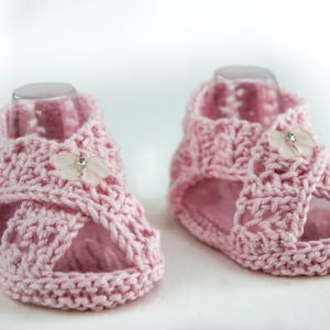 May include: A pair of pink crocheted baby sandals with a flower embellishment on each strap.