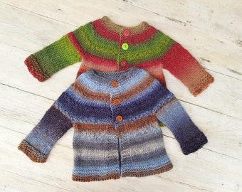May include: Two knitted baby cardigans with button fastenings. One cardigan is green, red, and brown with green buttons. The other cardigan is blue, brown, and grey with brown buttons.