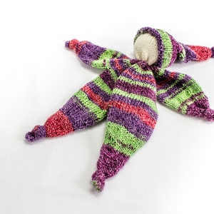May include: A handmade knitted doll with a striped purple, green, and red outfit. The doll has a white fabric head and a knitted hat.