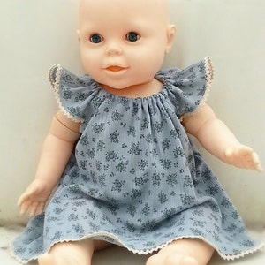 May include: A porcelain baby doll wearing a blue and white floral dress with a lace trim.