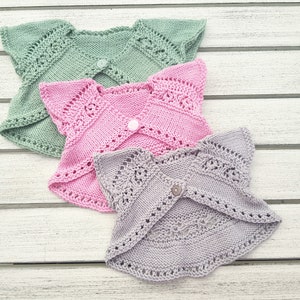 May include: Three knitted baby cardigans in different colors: green, pink, and gray. Each cardigan has a delicate lace pattern and a button closure.