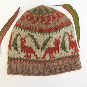 May include: A brown, green, and orange knitted hat with a pattern of stylized animals. The hat has a fold-over cuff.