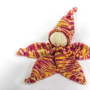 May include: A knitted doll with a striped hat and matching outfit in shades of pink, yellow, and white.