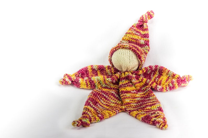 May include: A knitted doll with a striped hat and matching outfit in shades of pink, yellow, and white.