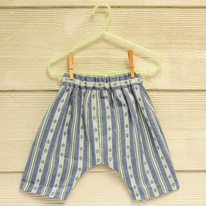 May include: Blue and white striped pants with a green sailboat pattern hanging on a wooden hanger.
