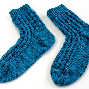 Puede incluir: Un par de calcetines azules de punto con un patr&oacute;n texturizado. Los calcetines est&aacute;n hechos con un hilo azul claro y tienen una franja azul oscuro que recorre el centro de cada calcet&iacute;n.