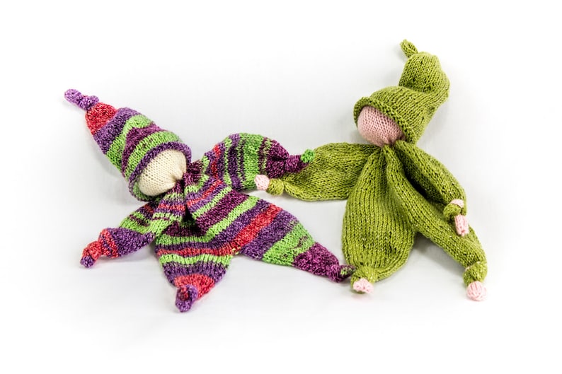 May include: Two knitted dolls, one in green and one in purple, green, and red stripes. Both dolls have a knitted hat and a white face.