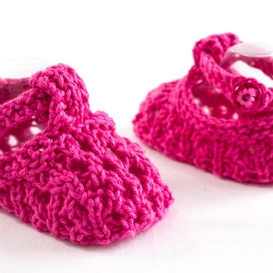 May include: A pair of pink crocheted baby shoes with a flower button detail.