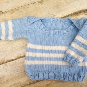 Könnte beinhalten: Hellblauer Baby-Pullover mit weißen Streifen auf Körper und Ärmeln. Der Strickpullover hat einen runden Halsausschnitt und lange Ärmel. Das Kleidungsstück ist aus weichem Garn gefertigt, ideal für ein Neugeborenes.